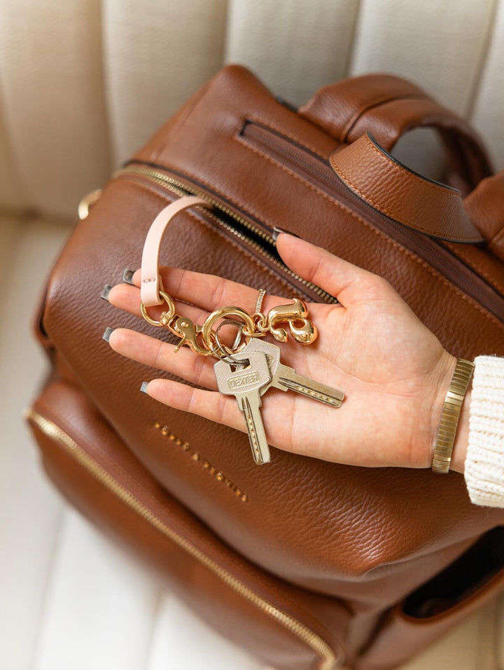 Poppy & Peonies The Cabin Backpack in Chestnut, close-up of a hand holding keys above the brown exterior, highlighting the gold-tone key leash.