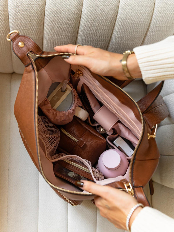 Poppy & Peonies The Cabin Backpack in Chestnut, overhead lifestyle view showing the open interior with blush-pink lining, organized compartments, a water bottle, and everyday essentials.