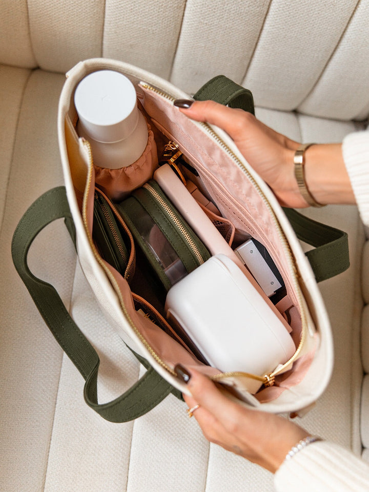 Poppy and Peonies The Small Signature Tote Olive shown from above with its cream canvas exterior, olive green straps, gold-tone zipper, and blush pink interior featuring organized compartments filled with a water bottle, accessory pouches, and everyday essentials.