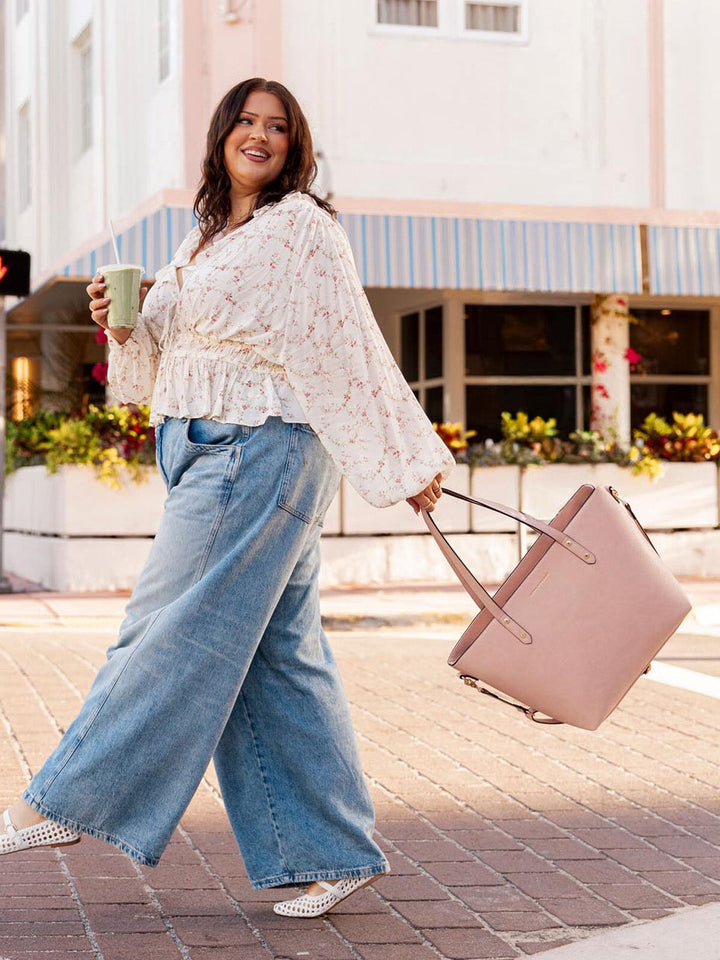 Woman walking outdoors holding a light pink tote bag and a green cup.