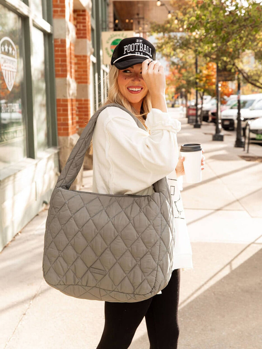 Woman holding a quilted gray bag and a coffee cup on a city street.