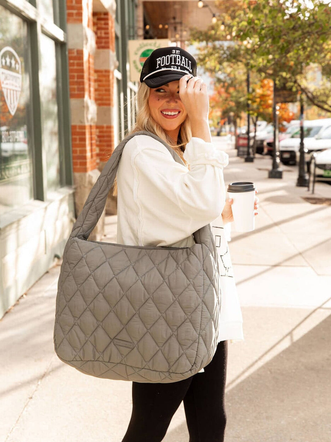 Woman holding a quilted gray bag and a coffee cup on a city street.