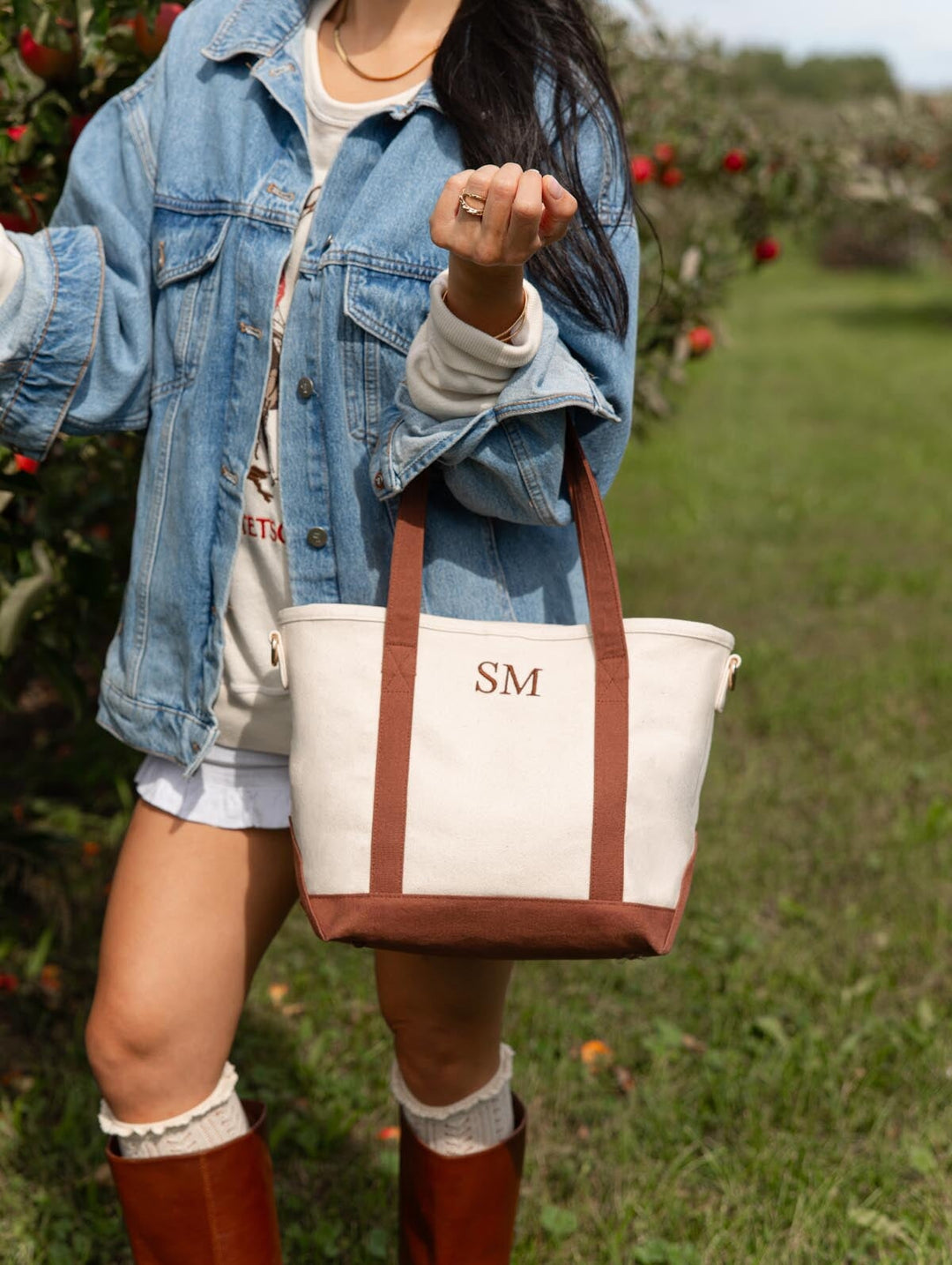 Close-up of Poppy & Peonies The Small Signature Tote in Chestnut carried by its brown handles, showing personalized initials against the cream canvas.