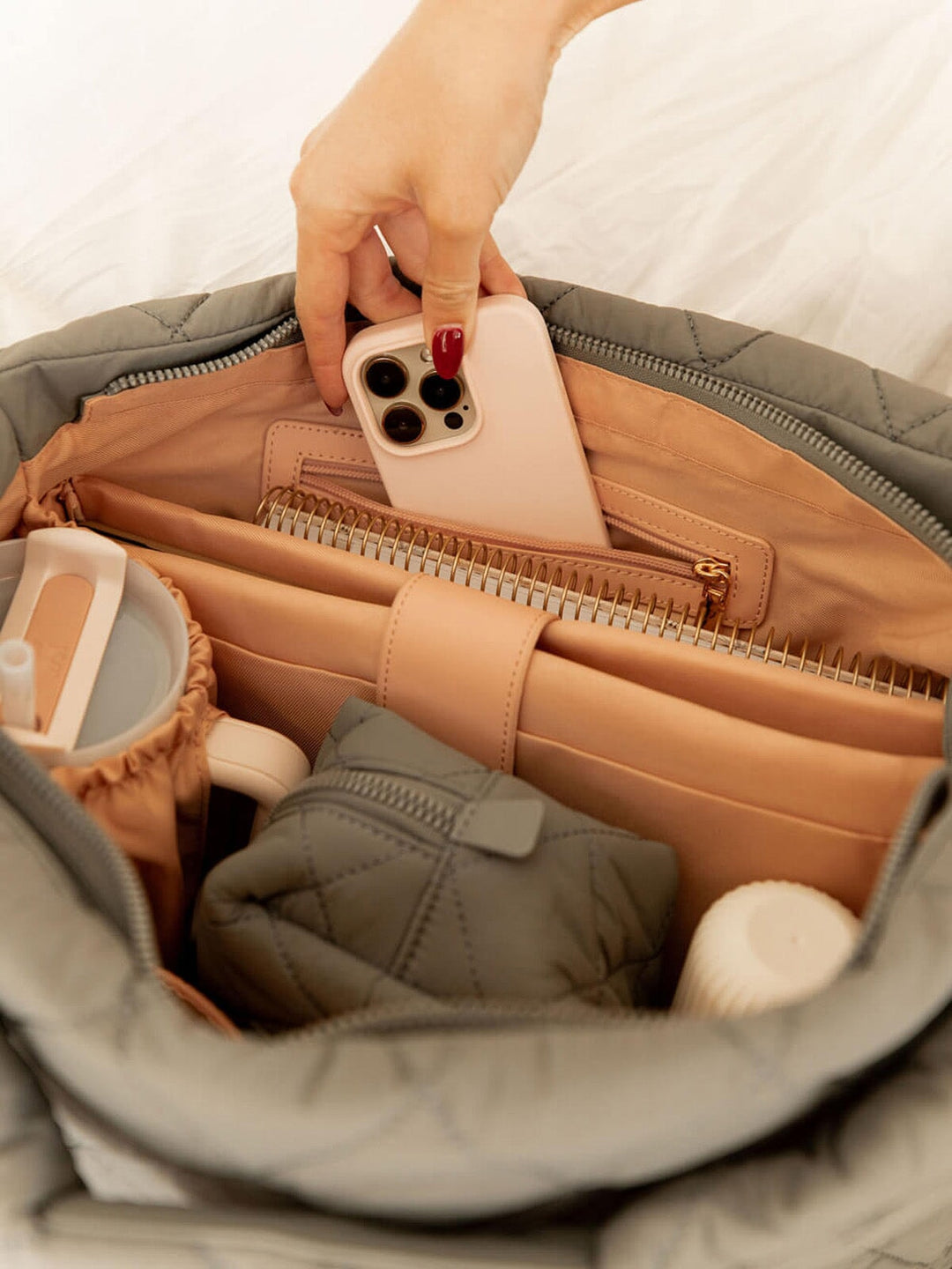 Person placing a phone into a quilted grey hobo bag with various items inside