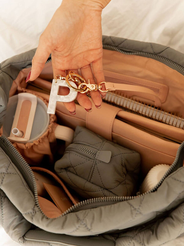 Person holding a keychain with a letter 'P' in front of an open quilted hobo bag.