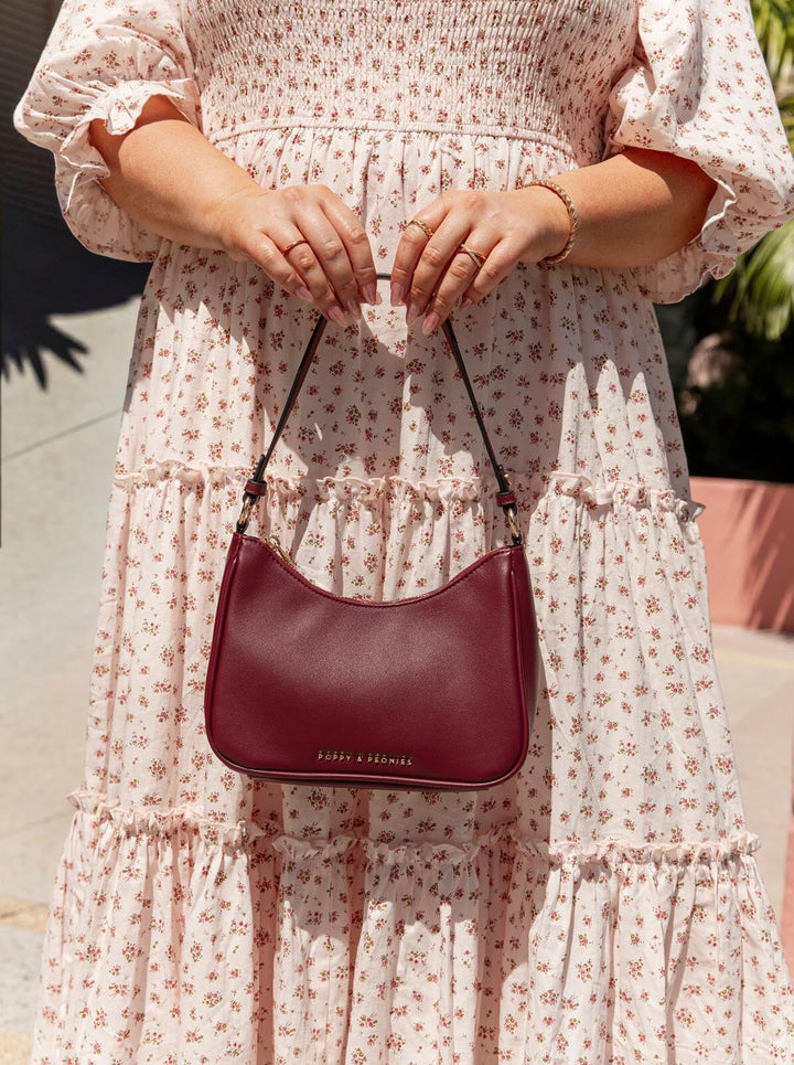 Person wearing a floral dress holding a berry coloured handbag.