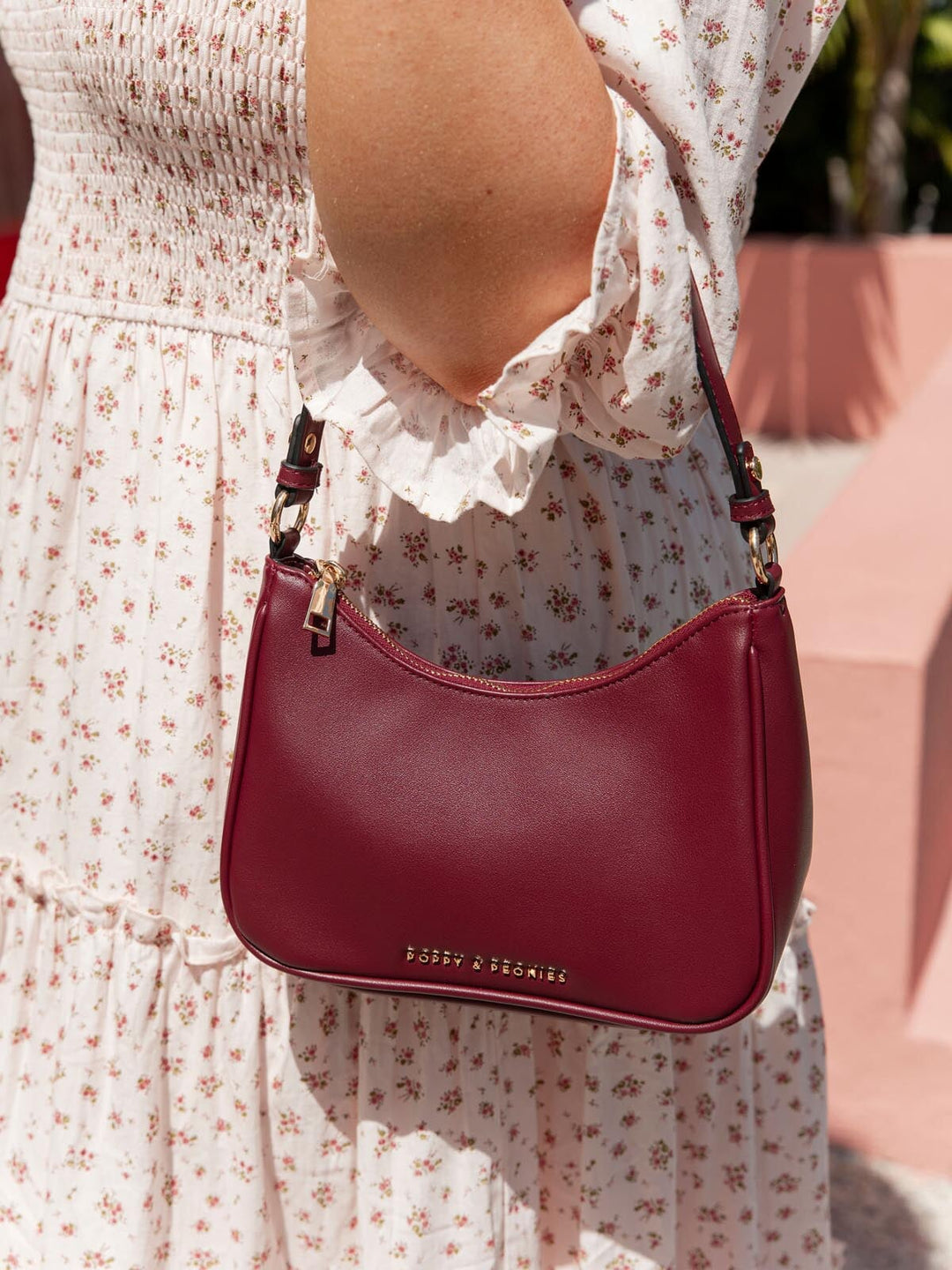 Person wearing a floral dress holding a berry coloured shoulder bag.