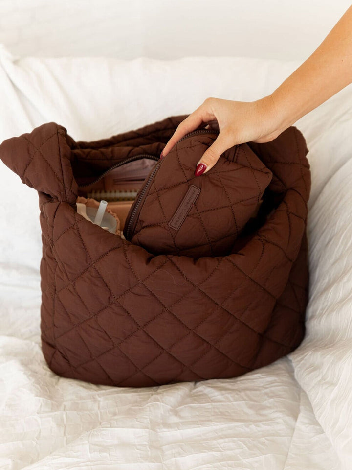 Brown quilted handbag with a hand reaching in to pull out a smaller bag on a white surface.