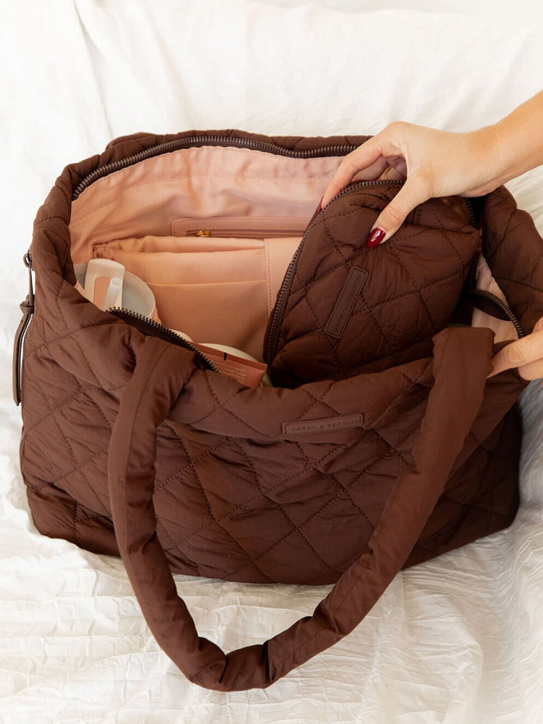 Brown quilted tote bag with a hand opening it on a white background