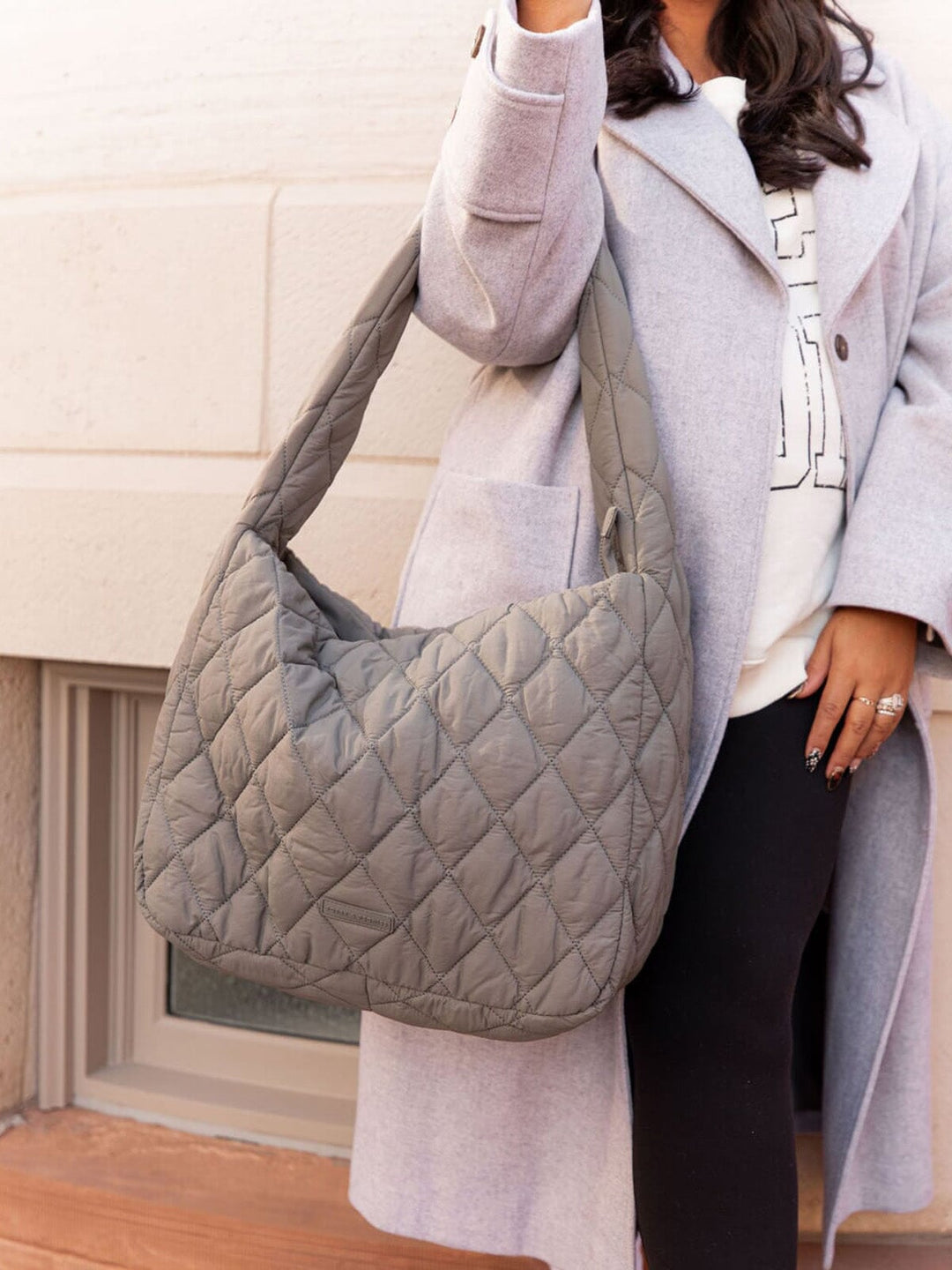 Person wearing a grey quilted handbag with a neutral background