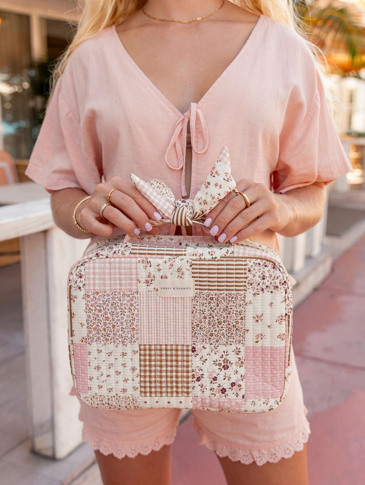 Person holding a patchwork toiletry bag with a decorative bow outdoors.