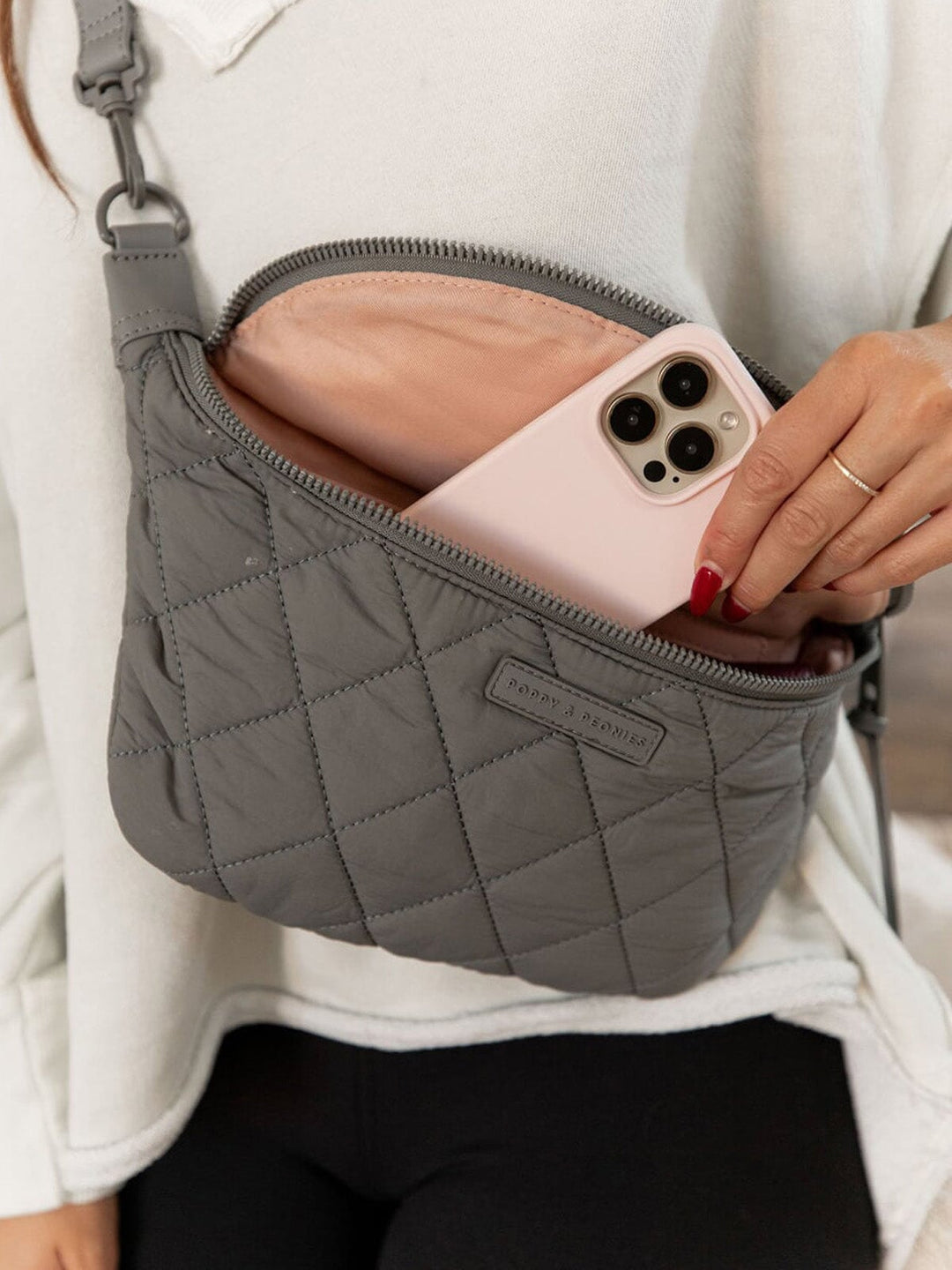 Grey quilted handbag with a phone inside, held by a person wearing a light gray sweater.