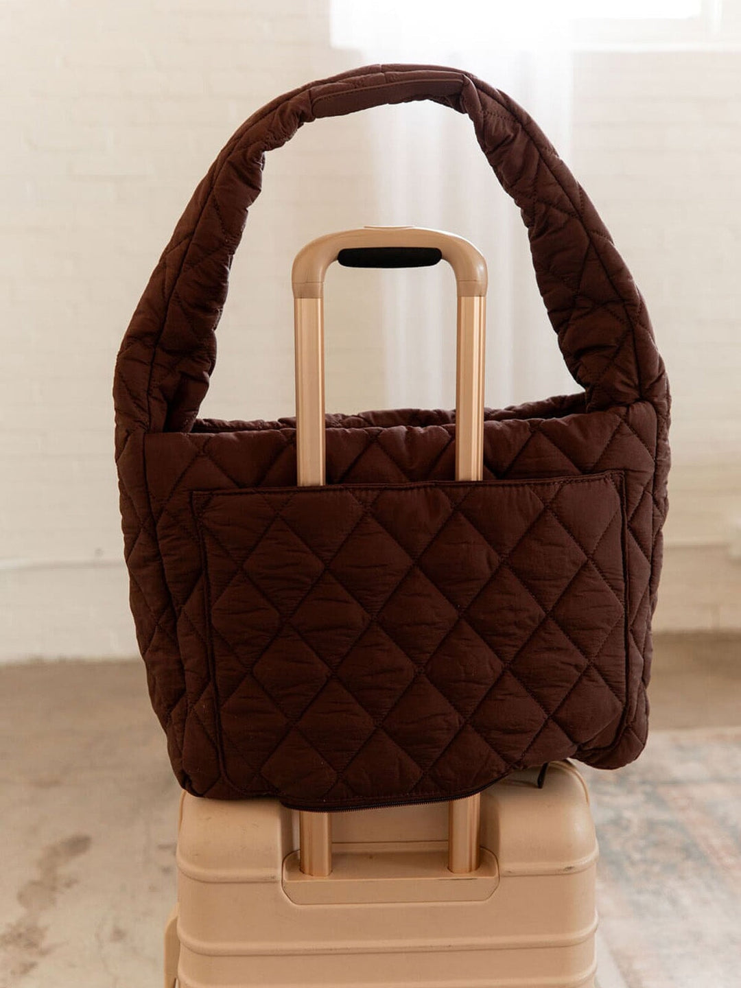 Brown quilted handbag with a trolley sleeve on a suitcase.