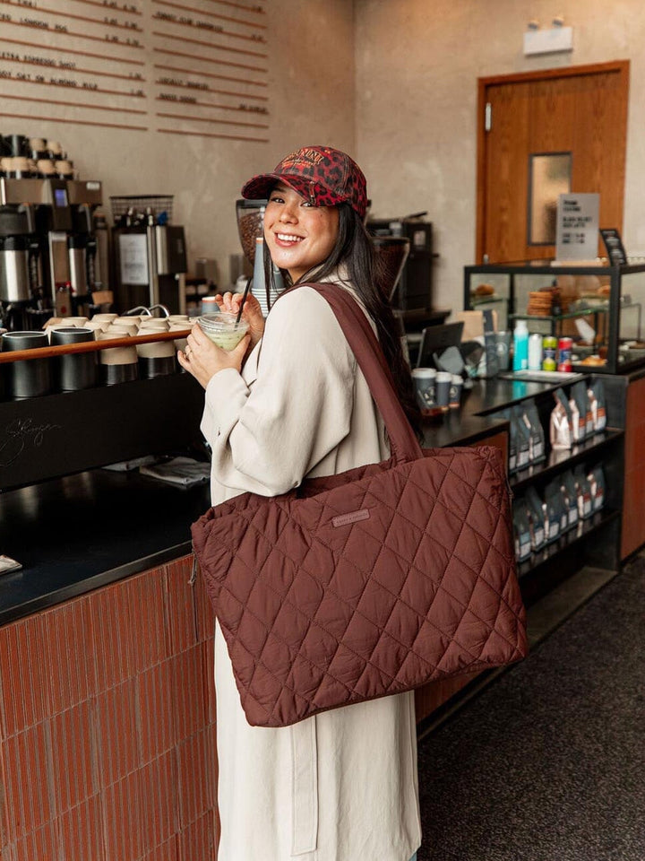 Woman holding a quilted brown tote bag in a coffee shop.