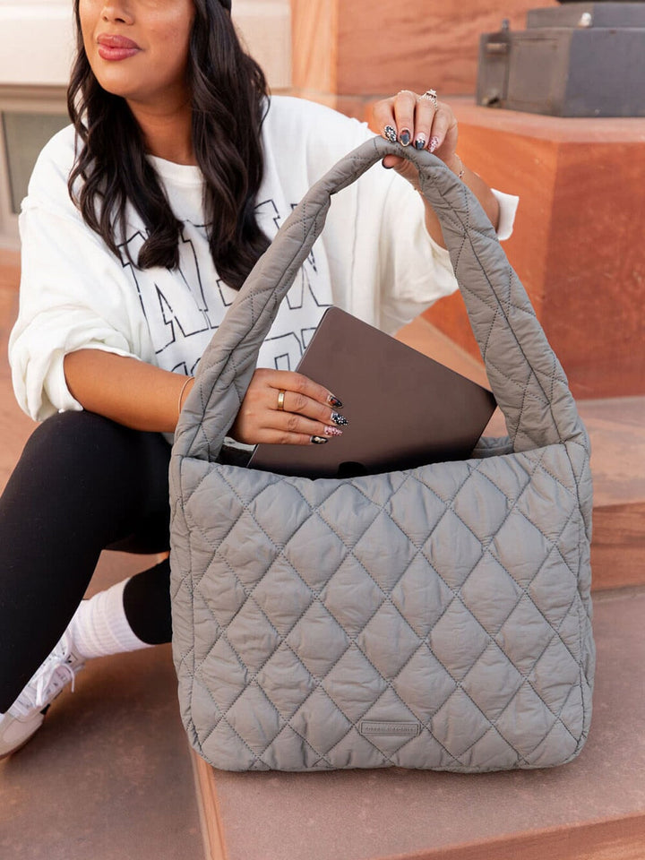 Woman holding a grey quilted handbag sitting on a wooden bench.