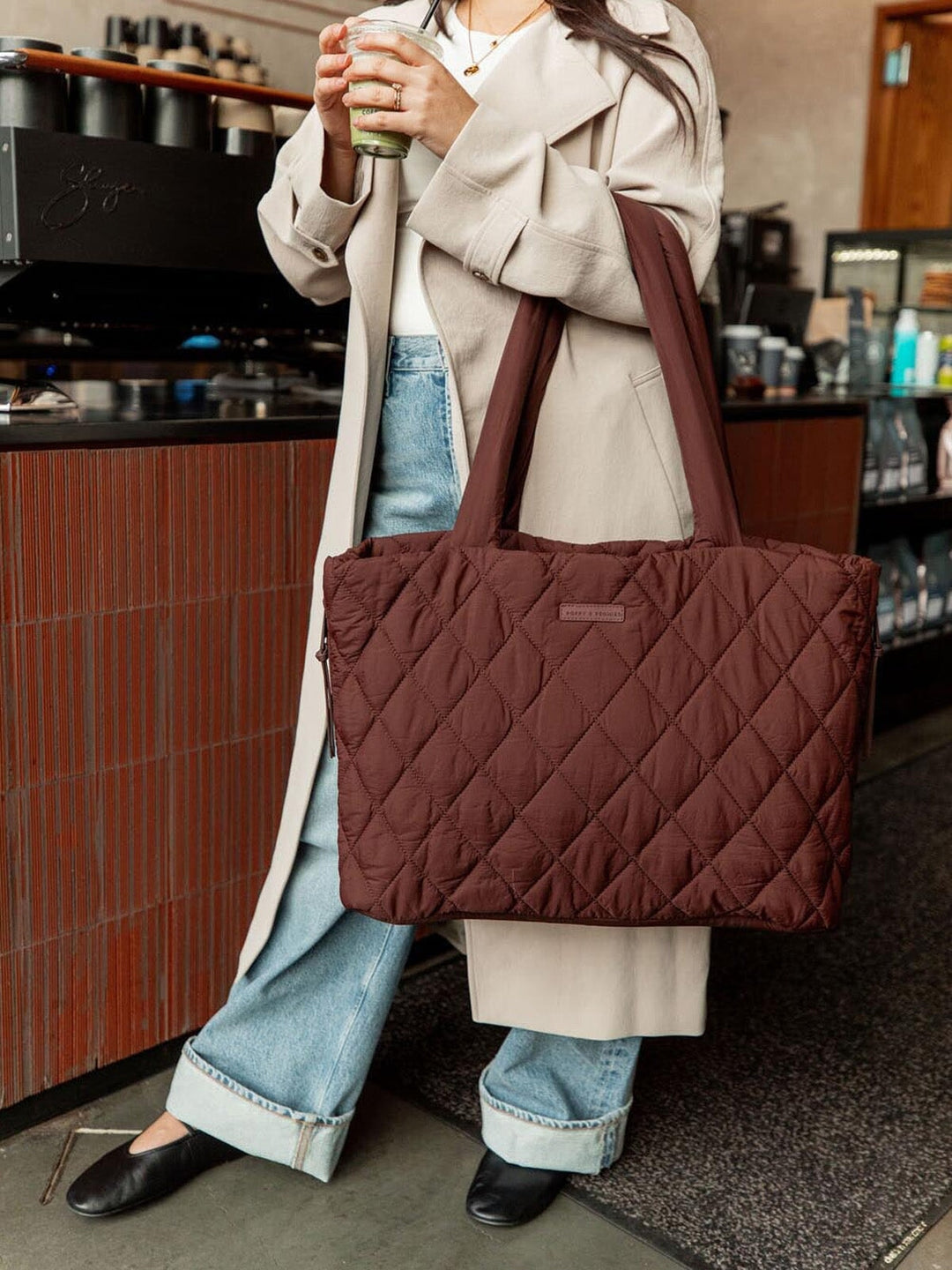 Person holding a brown quilted tote bag in a coffee shop setting